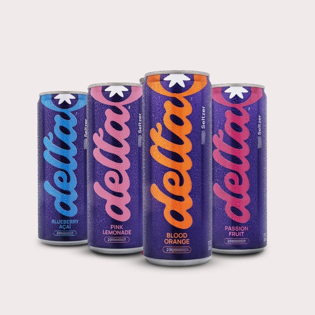 The Delta 20mg lineup: Blueberry Acai, Pink Lemonade, Blood Orange, and Passion Fruit cans, deep purple bodies with each flavor's signature script delta logo, cold and condensation-beaded on a soft cream background.